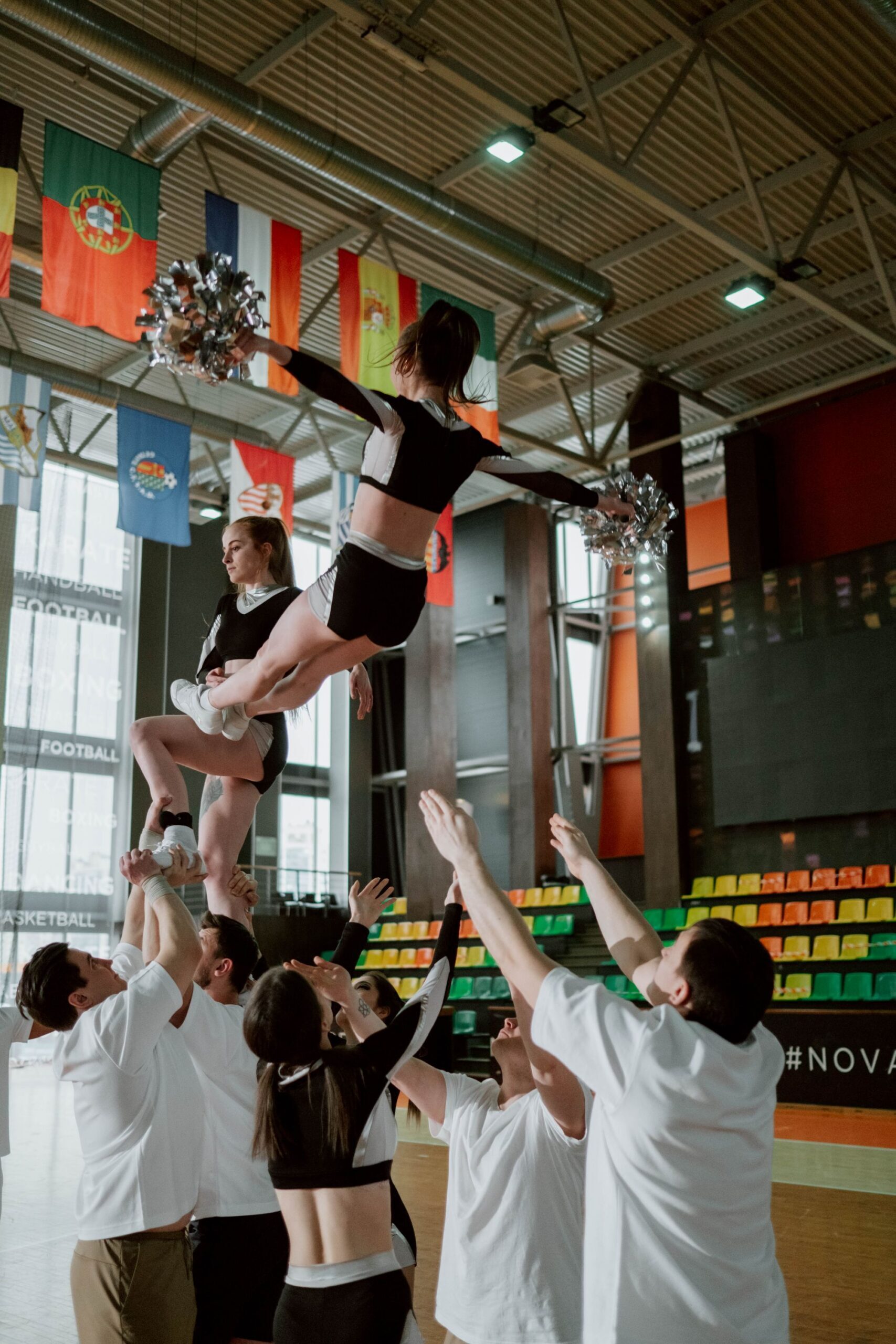 Cheerleaders performing a stunt in a gym under international flags