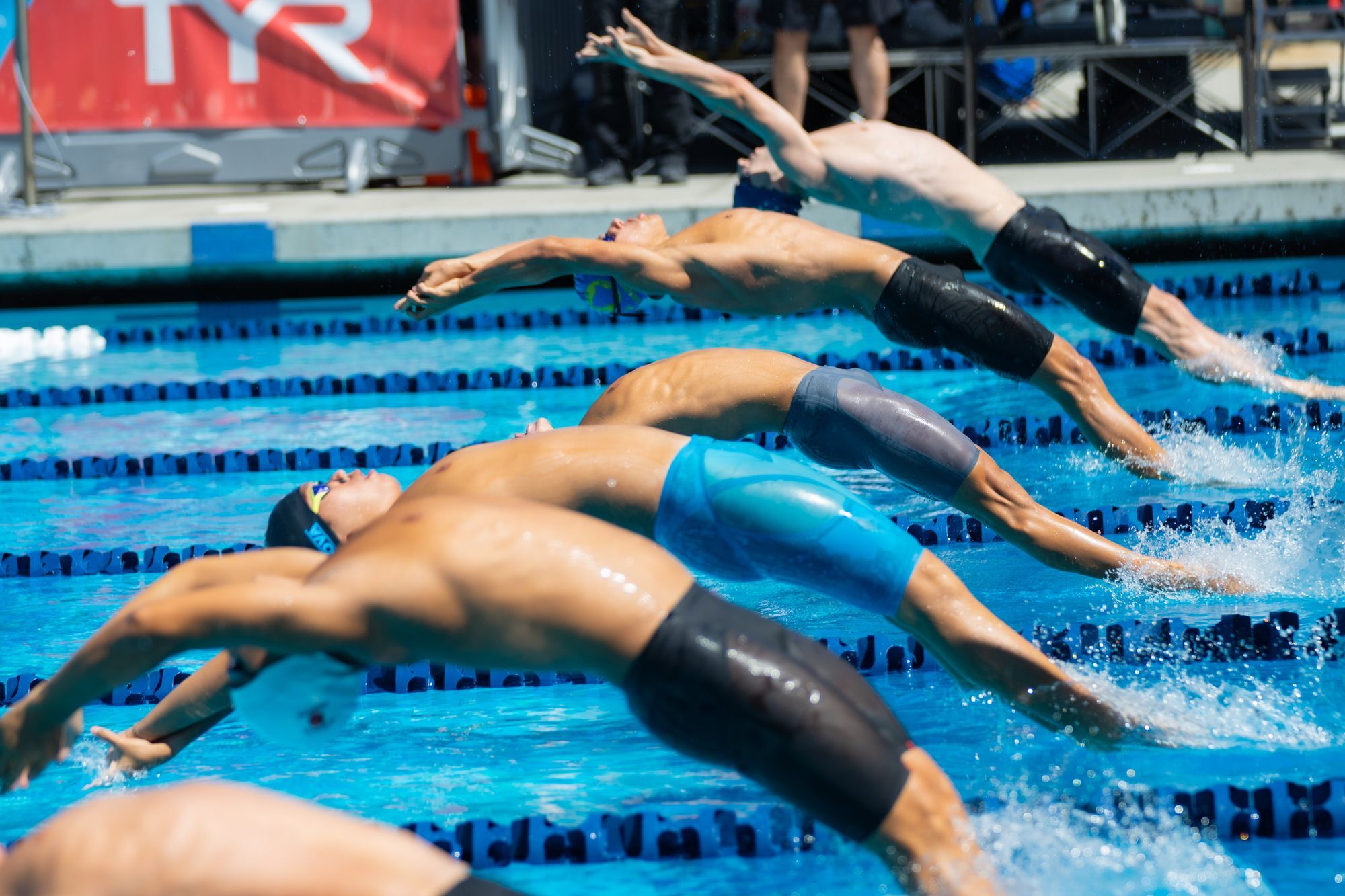 Swimmers diving into the pool at the start of a backstroke race