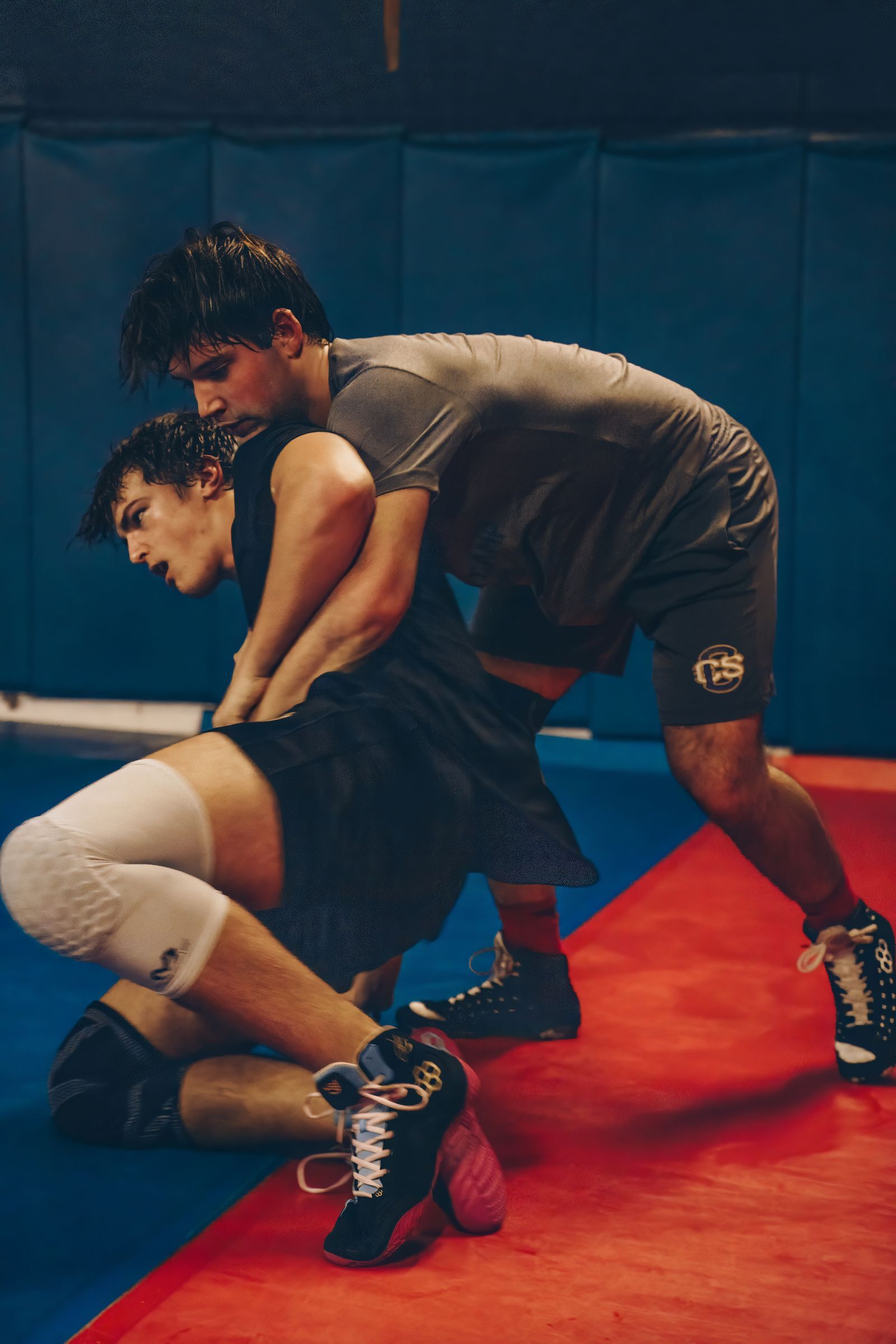 Two wrestlers grappling on a mat in a gym