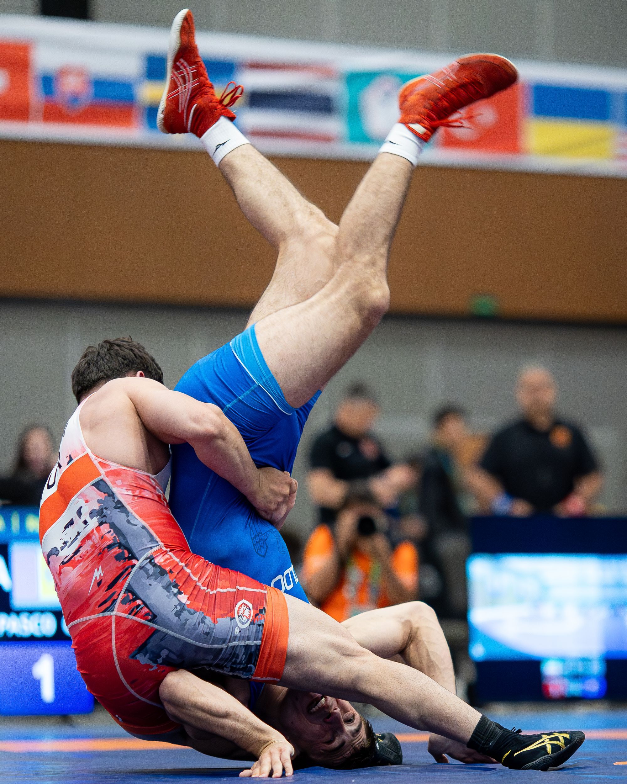 Two wrestlers competing in a match in front of a scoreboard and crowd